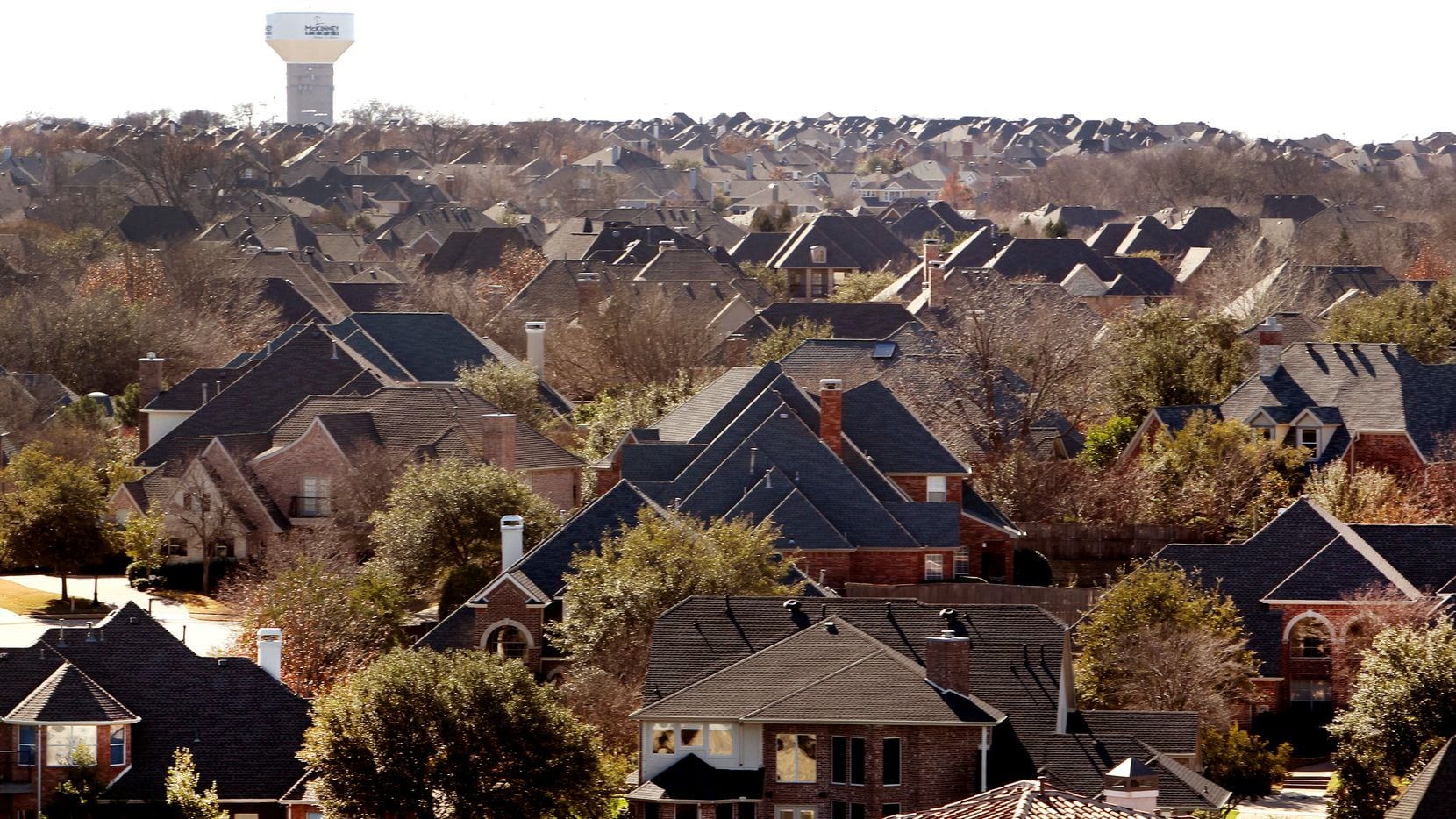 A McKinney water tower rises in the background over a sea of suburban rooftops of subdivisions in McKinney.