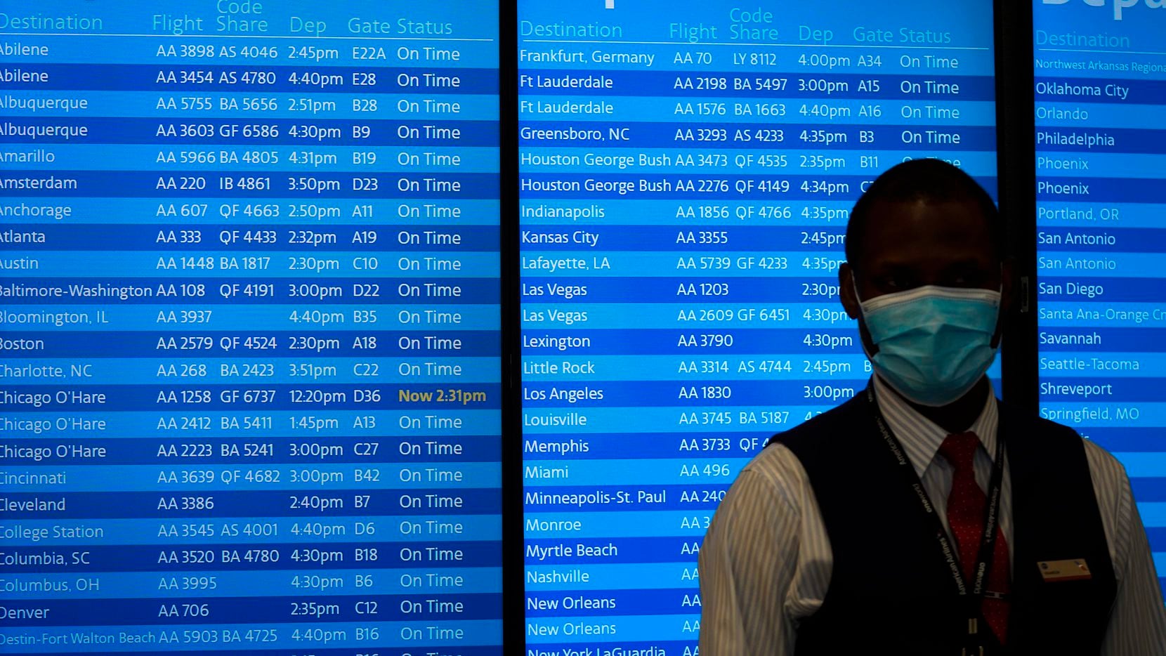 An American Airlines employee wears a face mask while standing in front of flight status...