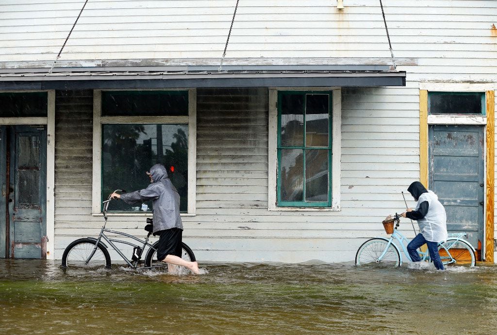 Jim Terrier (left) and Monica Grant of Galveston push their bikes along flooded Broadway...
