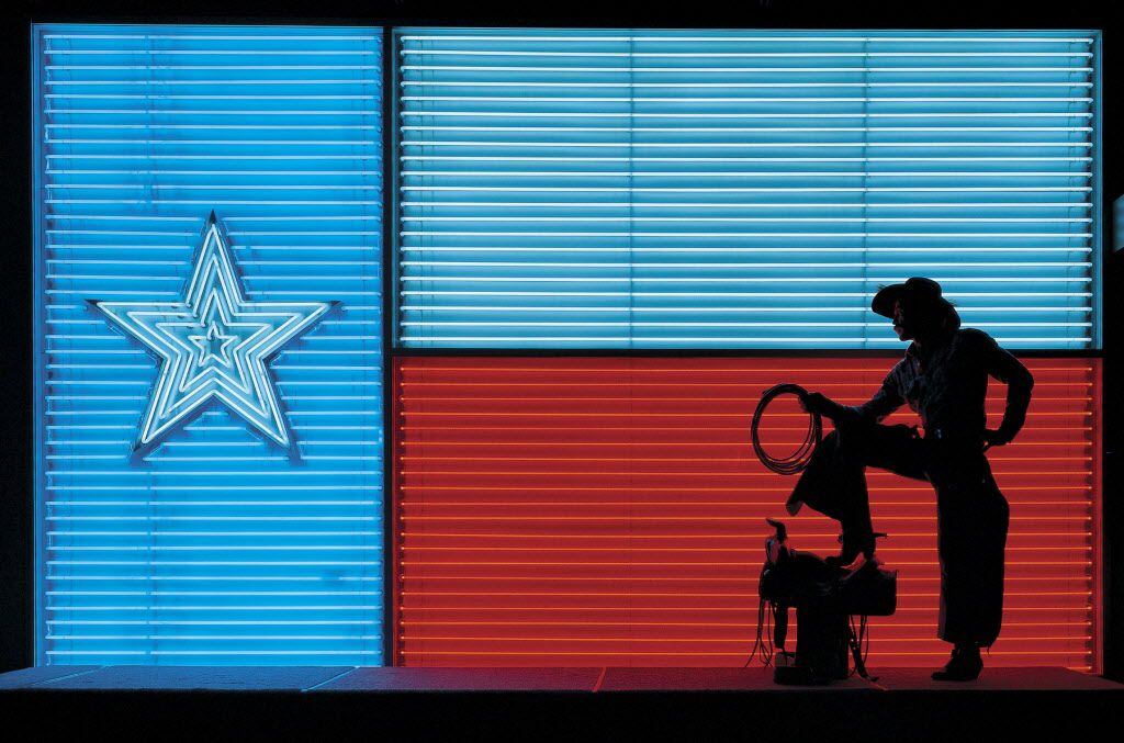 A cowboy poses in front of a neon version of the Texas flag at the Institute of Texan...