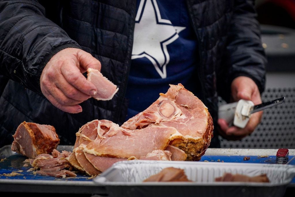 A fan carves a ham while tailgating before an NFL football game between the Dallas Cowboys...