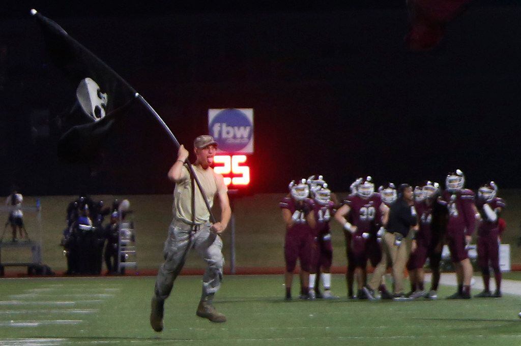 A Wylie student spirit squad member races onto the field with a flag sporting the school...