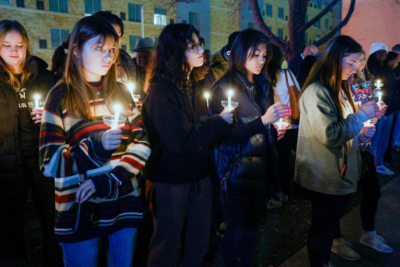 Community members hold candles during the playing of “Amazing Grace” at a candlelight vigil...