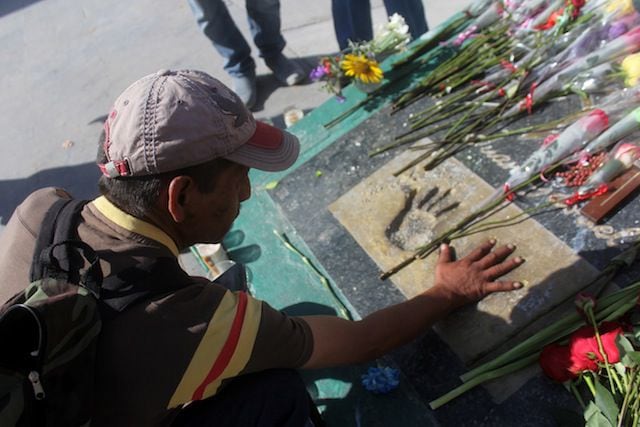 Un hombre coloca su mano sobre las huellas de Juan Gabriel en una placa frente al lugar...