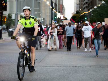A Dallas Police officer looks up as he rides a bicycle through the intersection of Main and...