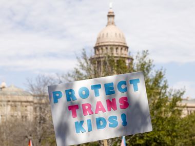 An attendee raises a “Protect Trans Kids” sign in front of the Texas State Capitol during...