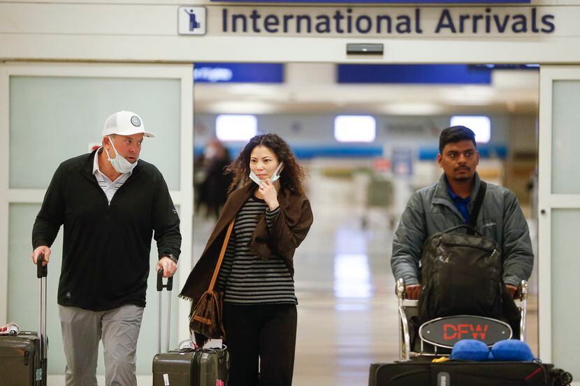 Travelers, some seen wearing protective masks, arrive in the international arrivals area of...