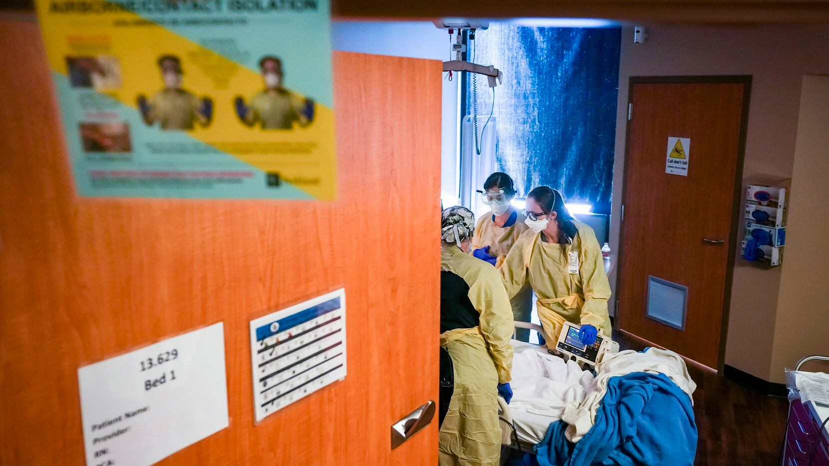 Los letreros sobre la entrada de un cuarto de hospital llevan instrucciones de protección para el personal médico mientras las enfermeras atienden a un paciente en la unidad de covid-19 en el Hospital Parkland, el miércoles, 5 de enero de 2022, en Dallas.