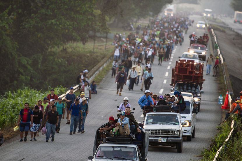 Migrantes hondureños caminan junto a vehículos que transportan a personas desde Chiapas,...