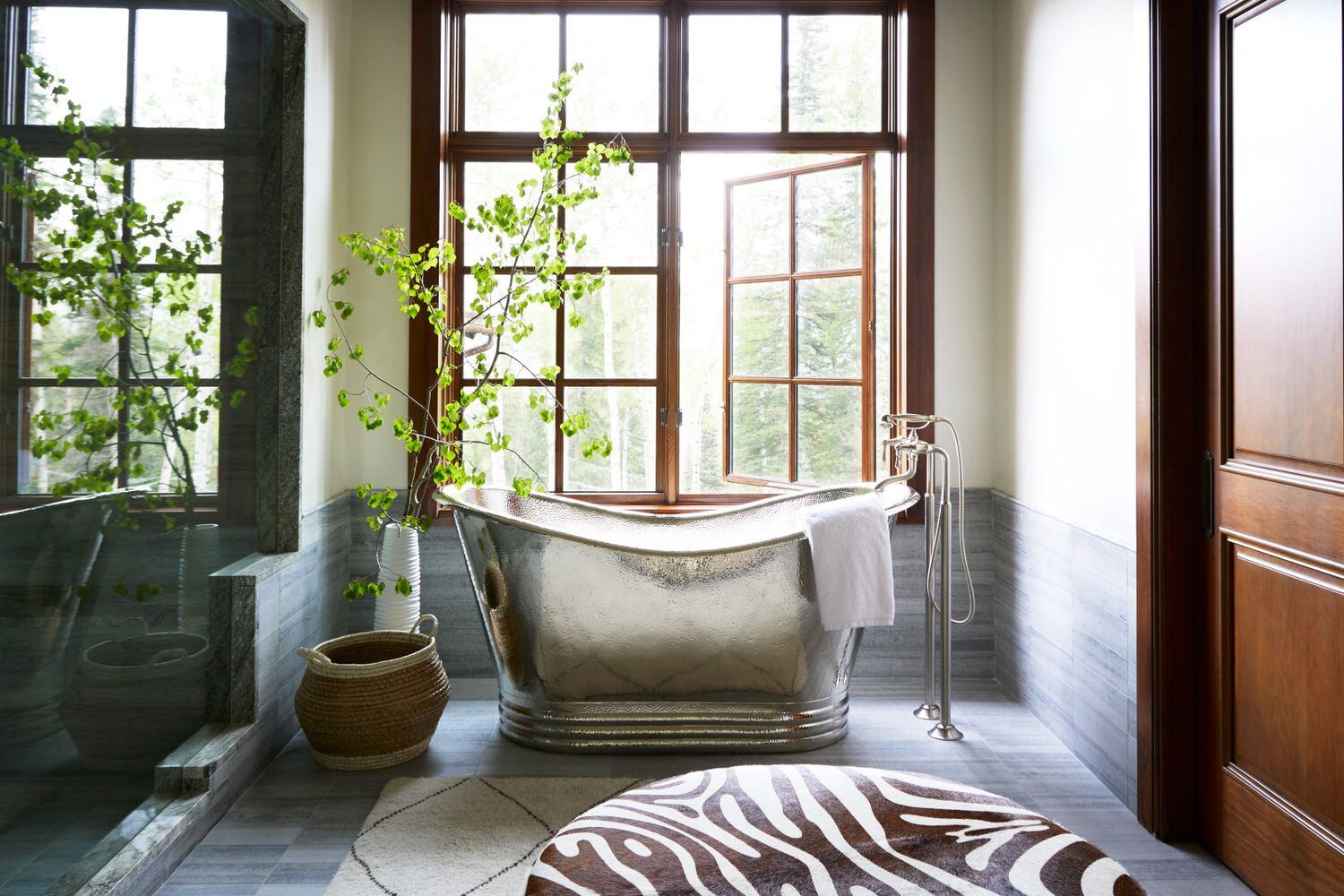Primary bathroom with large windows, silver freestanding tub and an animal-print ottoman
