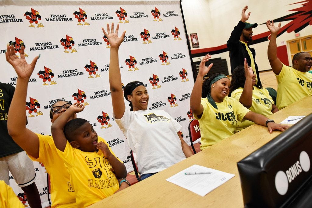 Irving MacArthur girls basketball players Hannah Gusters, center wearing white, and Sarah Andrews, at right, make the hand signal for the Baylor Bears after signing their letters of intent to play for Baylor University, Wednesday night Nov. 13, 2019 at Irving MacArthur High School in Irving. At left of Hannah is her mother Sheridane Gusters and brother Rylen Evans, 5. Right of Sarah is her parents Yolanda Ingram and Terry Woods, far-right.