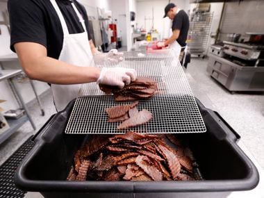 Frick Chanthorn removes warm beef jerky slices from the dehydration unit and piles them into container before flash frying them at Saap Lao Kitchen in Bedford.