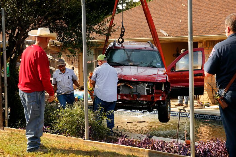 A wrecker crew uses a crane to lift a Jeep Grand Cherokee from a backyard pool on Clemson...