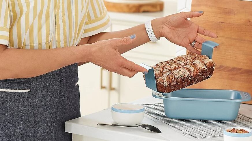 woman holding blue loaf pan with small cake in a kitchen