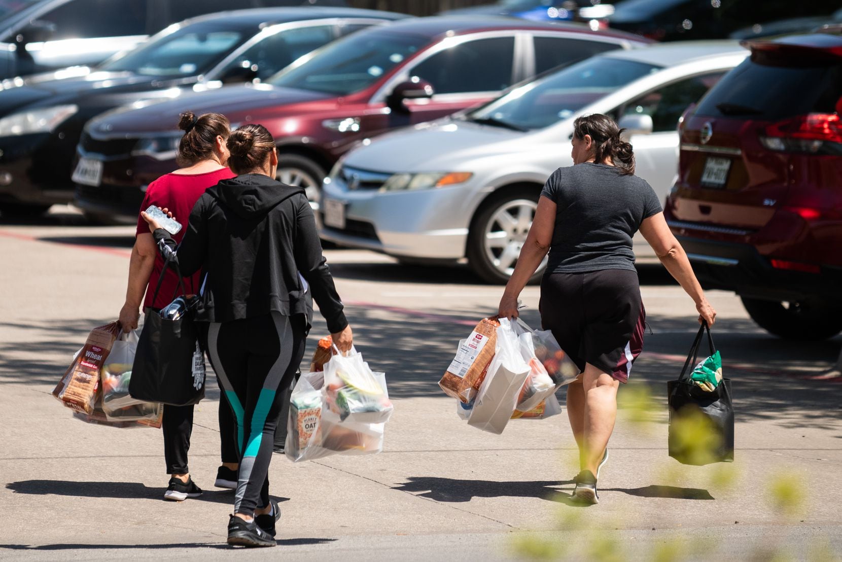 Women walk with bags of free groceries after attending a pop-up market and drive-through...