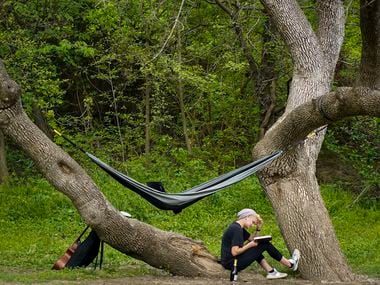 With a book, a hammock, a musical instrument, and a beverage, a woman enjoys time outdoors in Prairie Creek Park in Richardson, Texas.