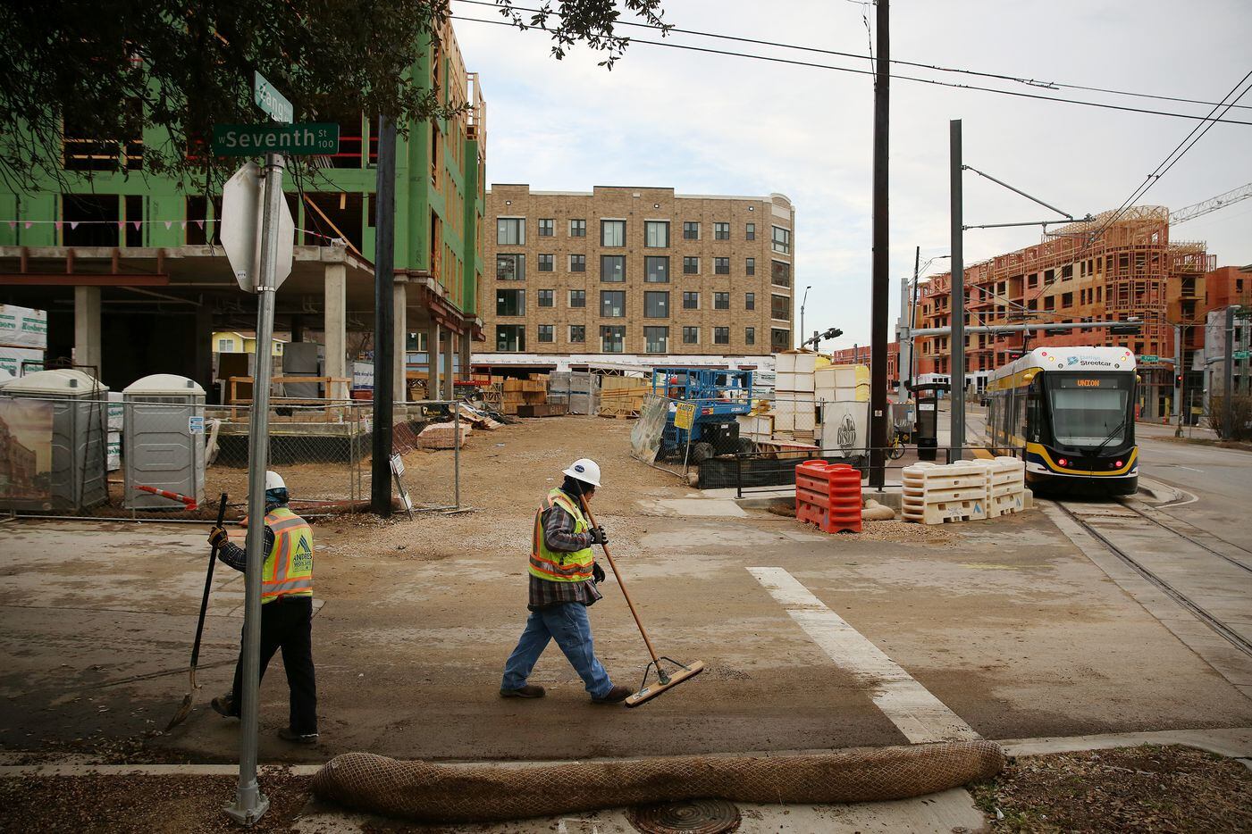 Ray Ramos (center), who grew up nearby close to Sunset High School, and a fellow laborer sweep near the corner of Seventh Street and Zang Boulevard across from the future property of Alamo Manhattan apartments. The Novel Bishop Arts apartments and the Alamo Manhattan apartments are being built across the street from each other at the corner of Zang Boulevard and Davis Street in the Oak Cliff neighborhood.