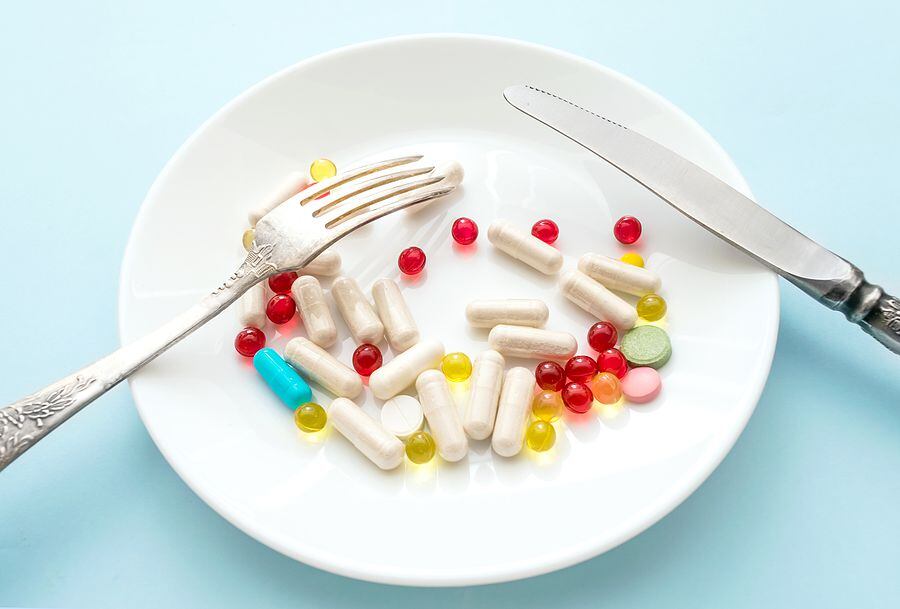 Many different weight loss pills and supplements as food on round white plate with fork and...