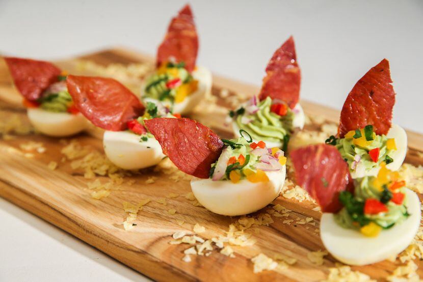 Avocado stuffed deviled eggs topped with baked prosciutto leaves