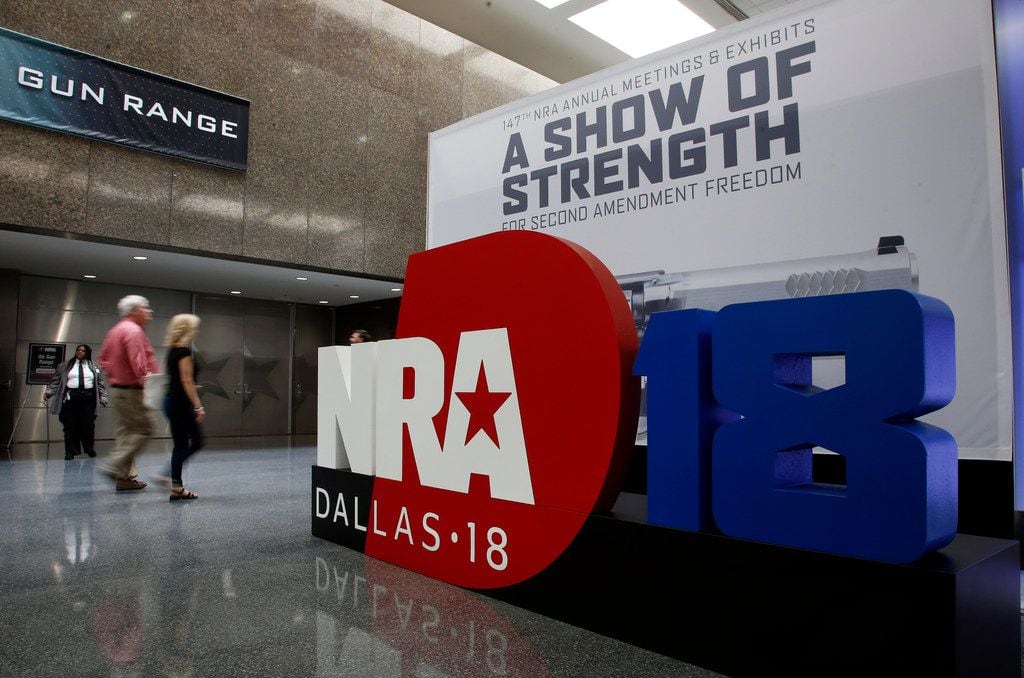 People walk by NRA convention signage in the Kay Bailey Hutchison Convention Center in...