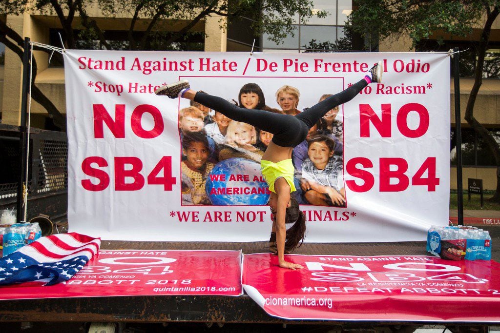Isabella Salinas, 10, does gymnastics in front of a sign in opposition to SB4 law, Texas' "sanctuary city" legislation, as opponents rally outside the  offices of State Rep. Matt Rinaldi on Wednesday, May 31, 2017, in Farmers Branch, Texas.