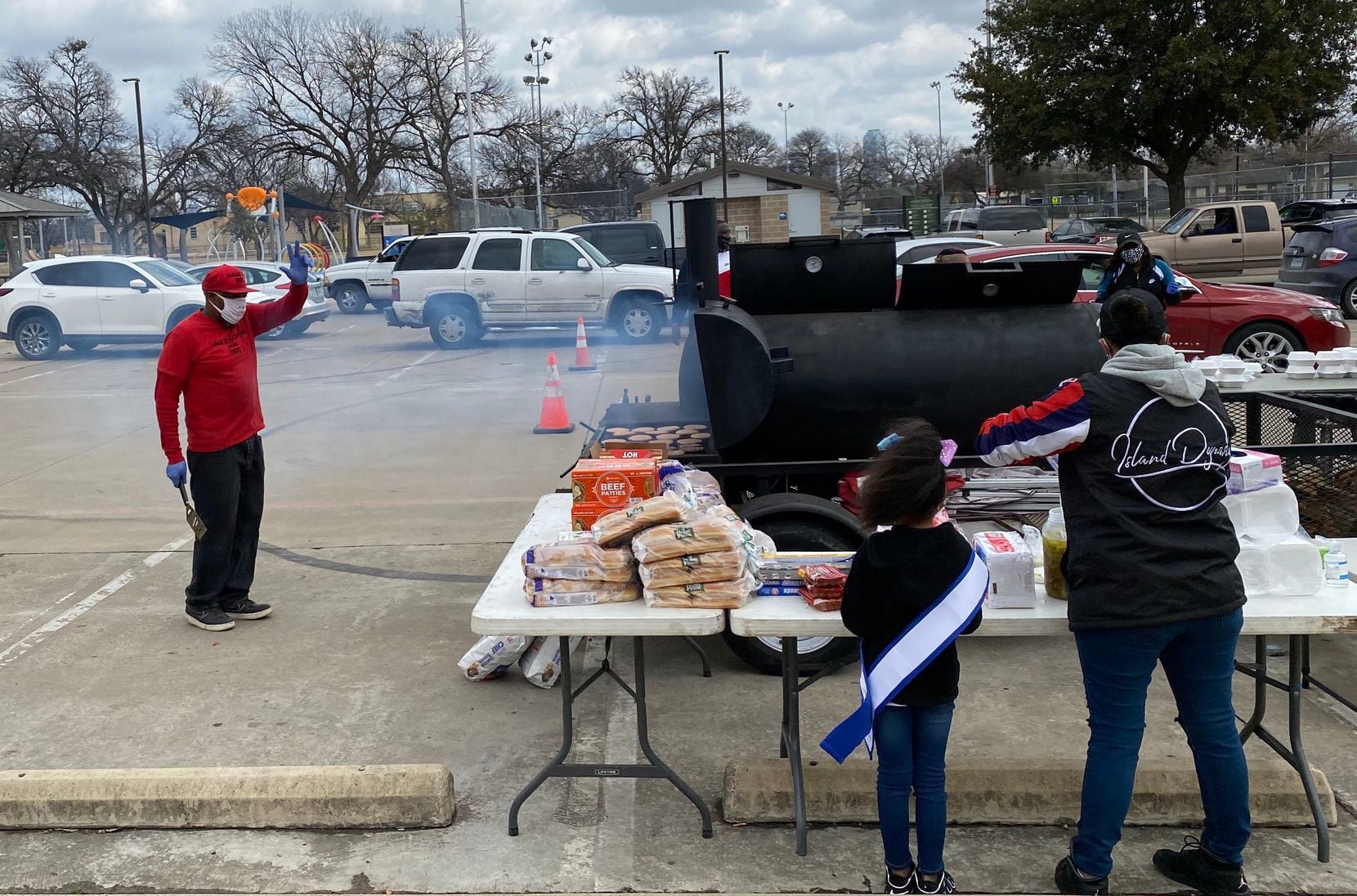 Tyrone Acy, 43, waves to volunteers at the water distribution site in West Dallas as he prepares burgers and hot dogs for families in need. Acy and his wife Erika own Mama 30's Off The Bone BBQ and were able to serve 300 hot meals Sunday.