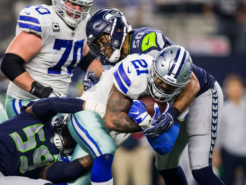Dallas Cowboys running back Ezekiel Elliott (21) is tackled by Seattle Seahawks linebacker Jake Martin (59) and Seattle Seahawks outside linebacker K.J. Wright (50) during the fourth quarter of an NFL playoff game between the Dallas Cowboys and the Seattle Seahawks on Saturday, January 5, 2019 at AT&T Stadium in Arlington, Texas.