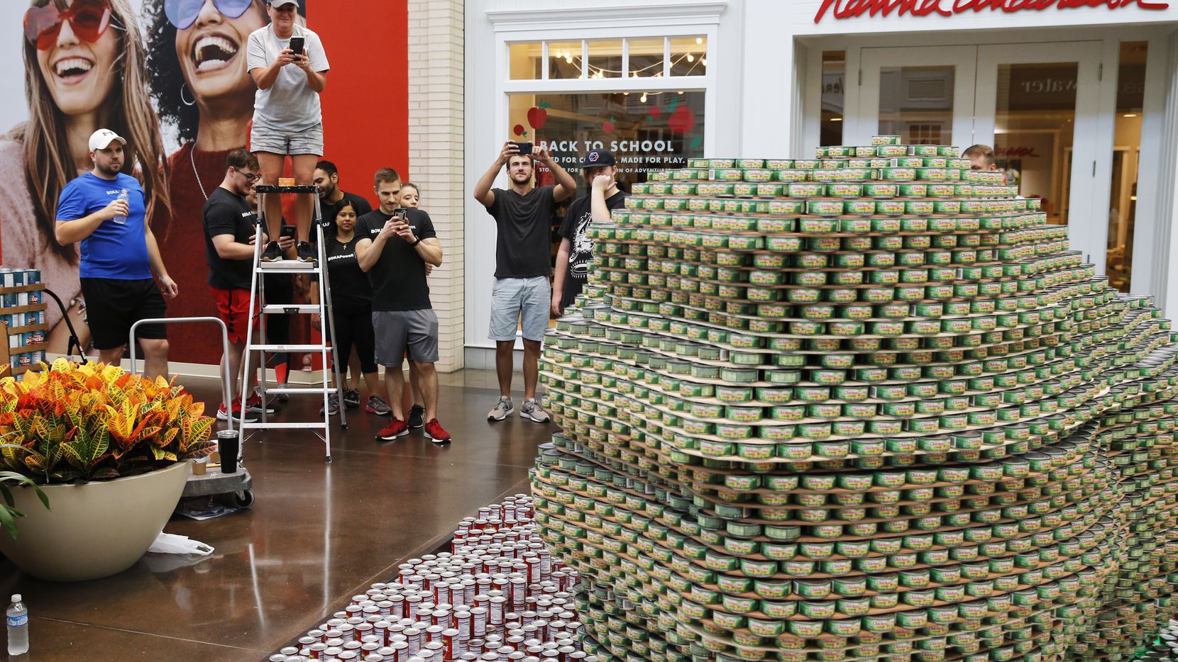 Shellie Gaffron of Ridgemont Commercial Construction uses a ladder to take a photo of the completed project as the company  teamed up with Boka Powell during the Canstruction charity event at NorthPark Center in Dallas in 2019.