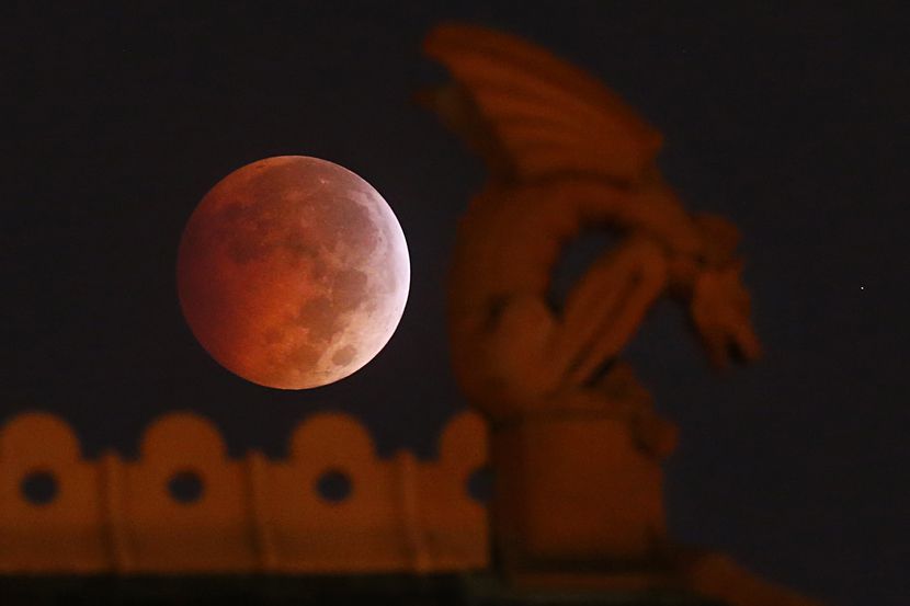 A blood moon appears behind a gargoyle atop the old red Dallas County Courthouse during a...