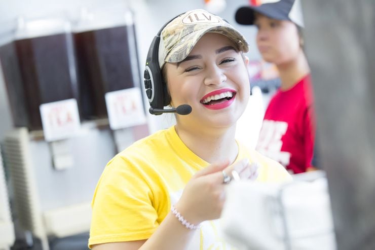 Raising Cane's employee in a yellow T-shirt and a headset holds a bag of food.