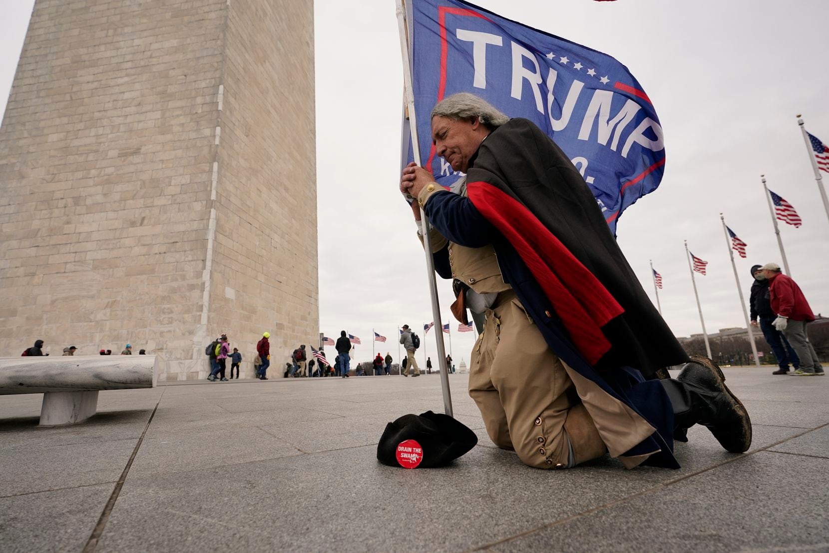 A man dressed as George Washington kneels and prays near the Washington Monument with a...