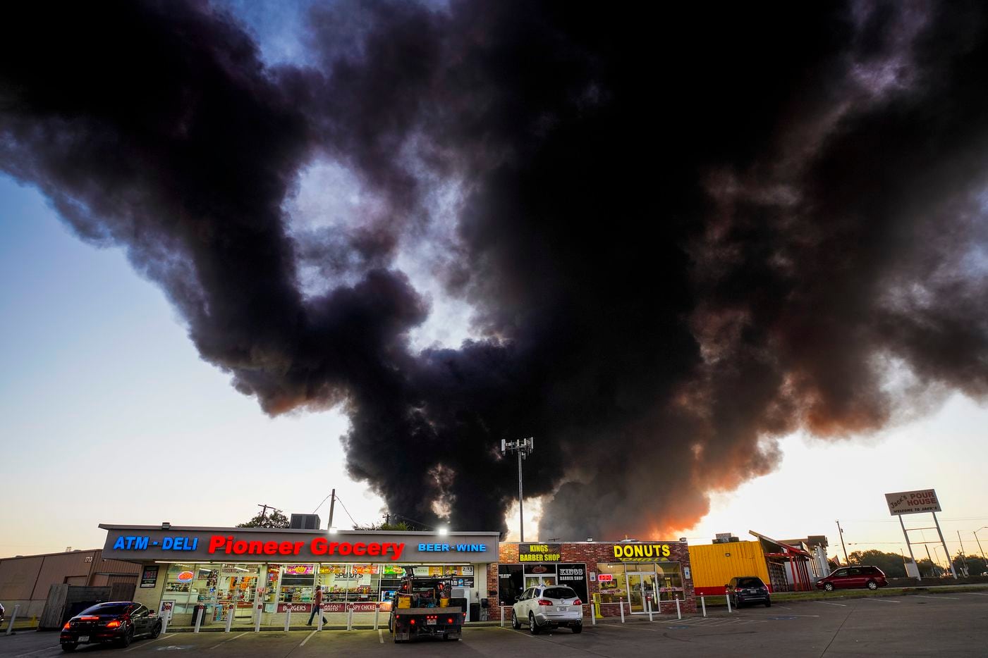 A plume of smoke rises over businesses at the corner of Great Southwest Parkway and Marshall Drive as fire crews battle a massive blaze in an industrial area of Grand Prairie just before sunrise on Wednesday, Aug. 19, 2020.