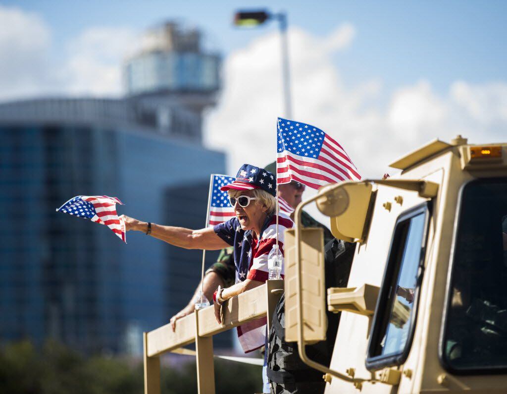 A woman waves an American flag from a military vehicle during the Dallas Veterans Day Parade...