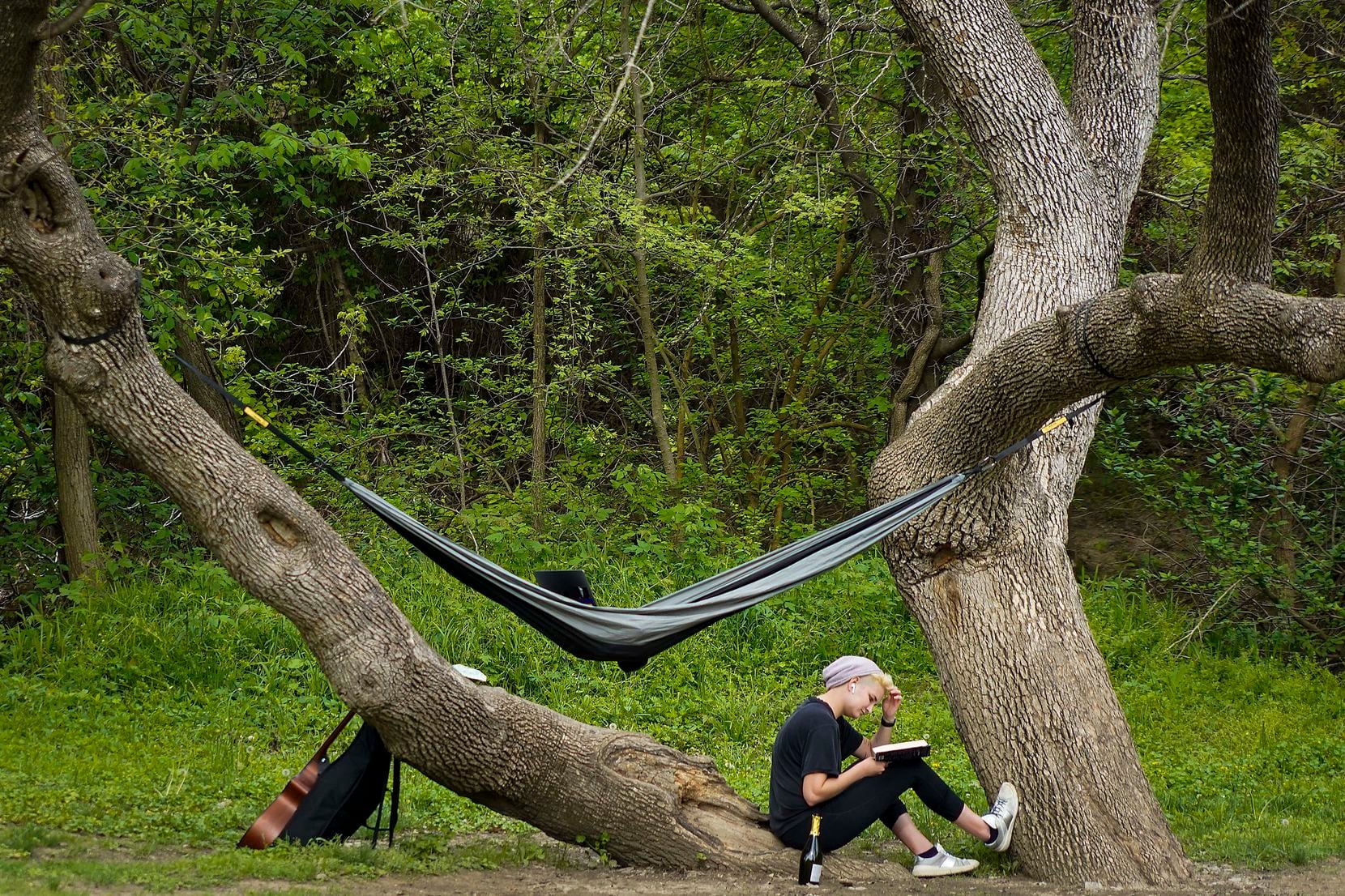 With a book, a hammock, a musical instrument and a beverage, a woman enjoys time outdoors in...