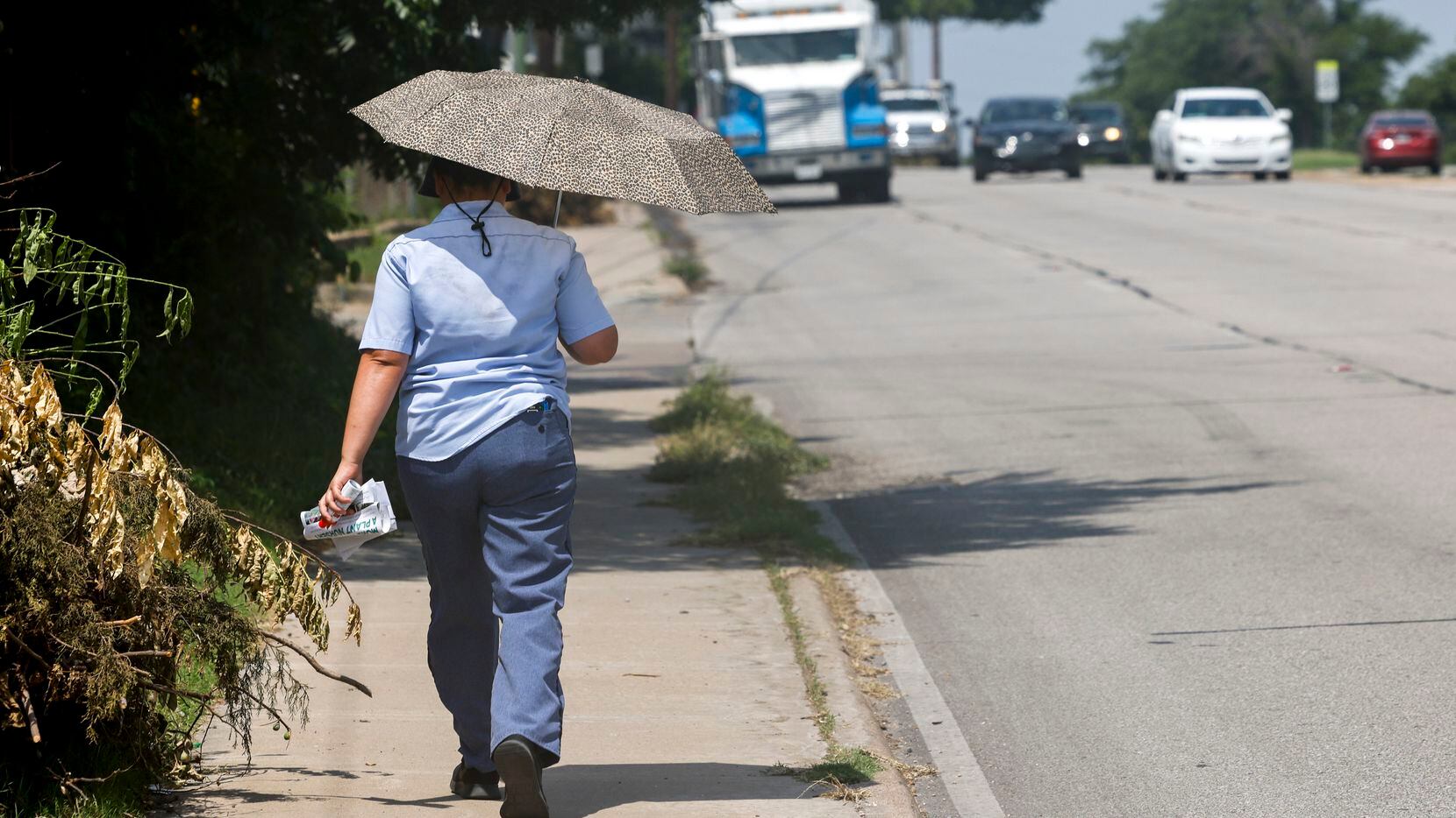 A U.S. Postal Service mail carrier tries to stay cool under the shade of an umbrella as she...