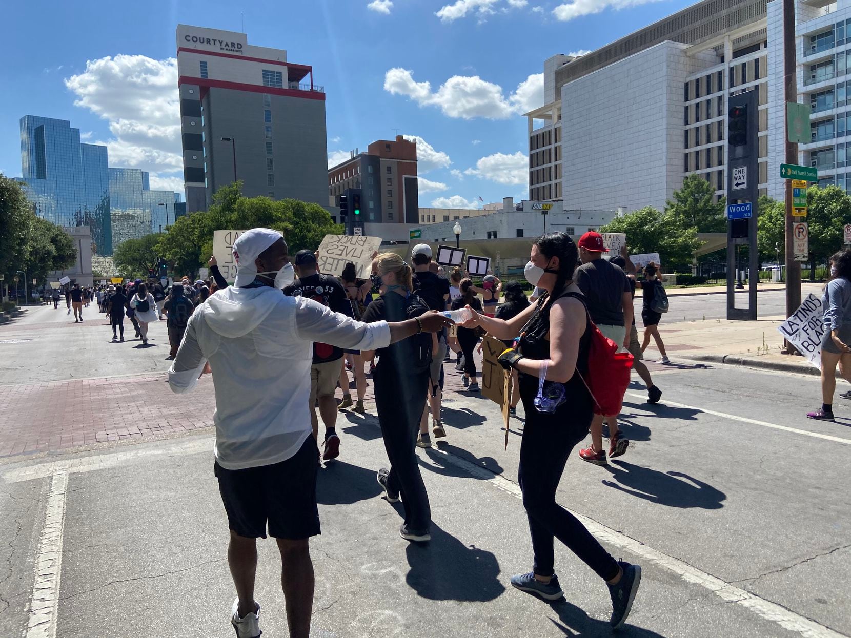 SMU running backs coach Ra'Shaad Samples passes out water bottles as protesters march along...