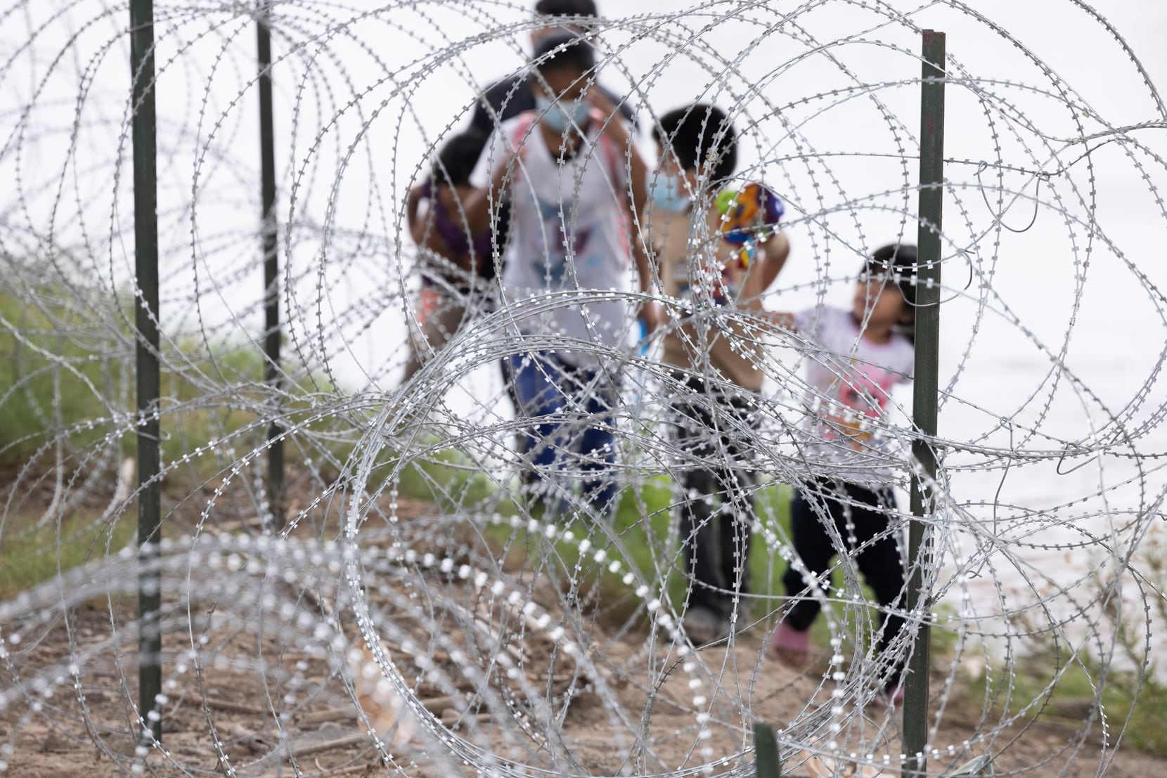 Migrants with children walk by razor wire fencing after crossing the Rio Grande River from...