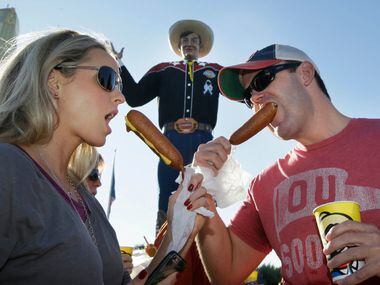 Gwin Huey, left, and her husband Ryan Huey eat corn dogs in front of Big Tex at the state...