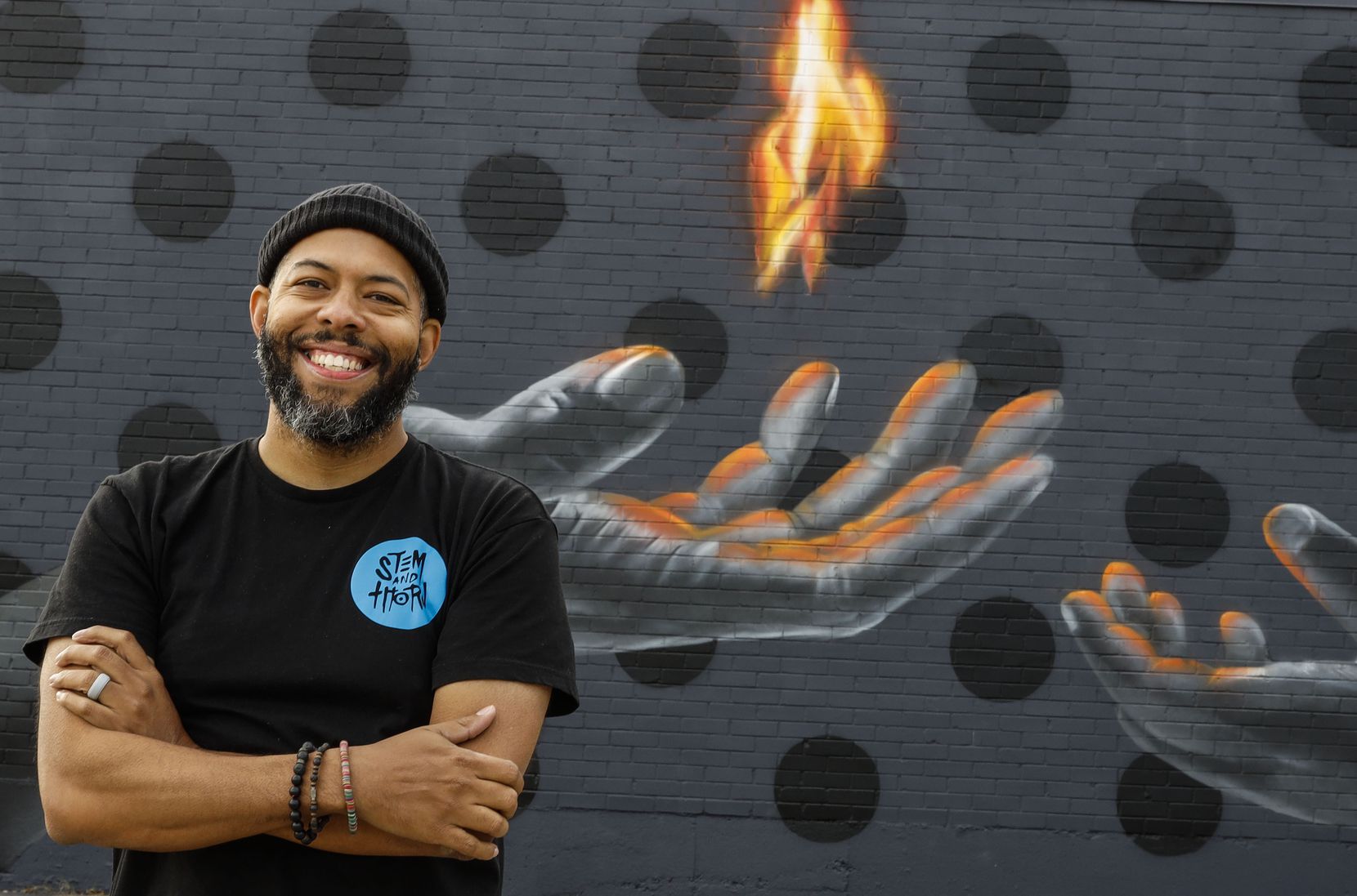 Jeremy Biggers posed for a portrait in front of his mural "Legacy" in Dallas on Nov. 18, 2021. The mural illustrates a flame passed from his hand to his 3-year-old daughter's hand. "A lot of murals that I work on are bread crumbs left to my daughter all over the city that are little love letters to her" Biggers says.
