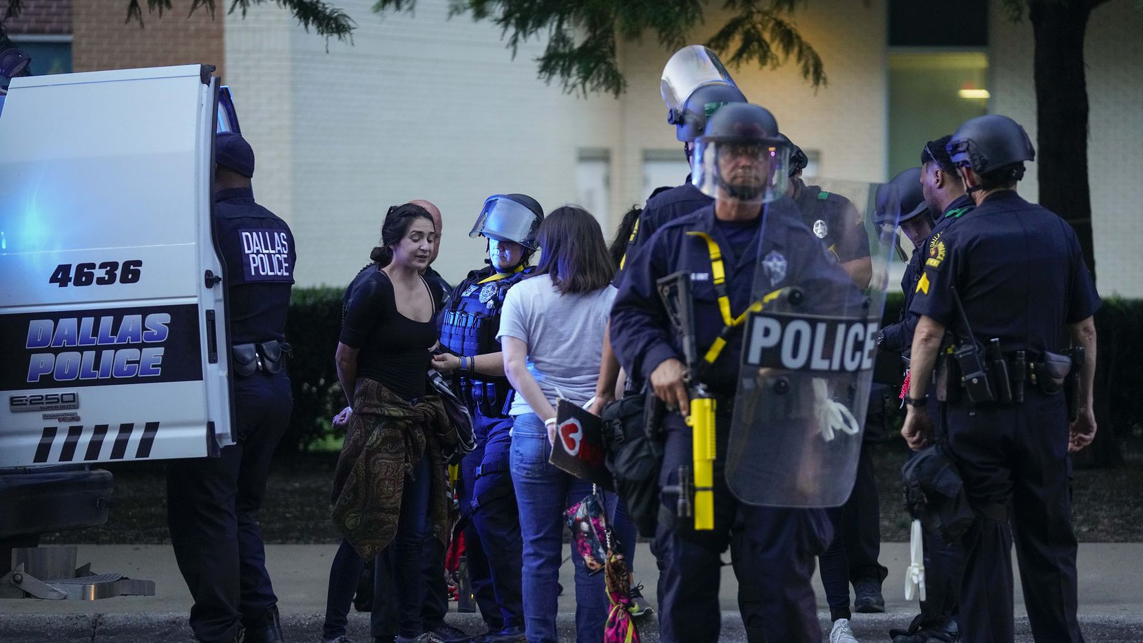 A group of people, some carrying protest signs, are arrested for curfew violations outside...