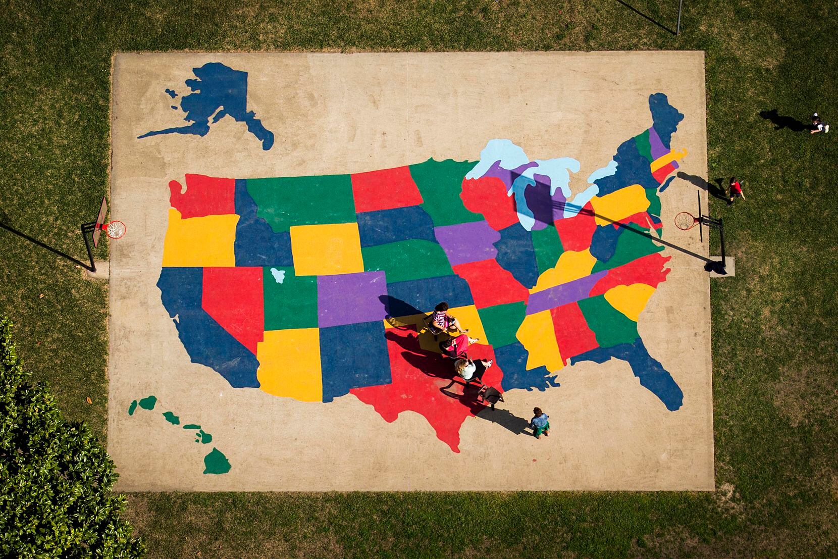 A playground map of the United Statse provides the background as adults watch children play...