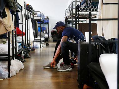 Isaac Amos prepares for work by putting his shoes on in the emergency shelter room of the...
