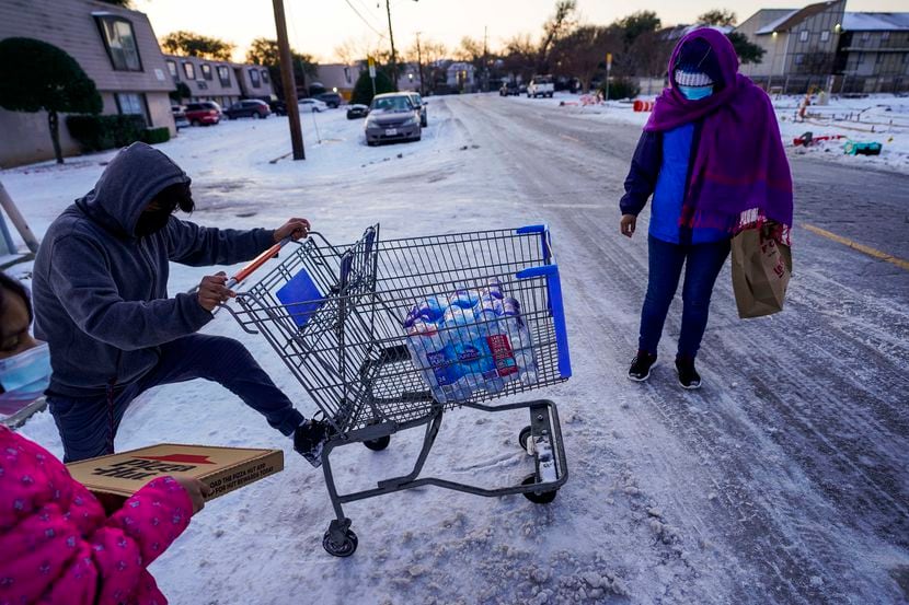 Juan Carlos Gonzalez pushes a shopping cart with two cases of drinking water, distributed at...