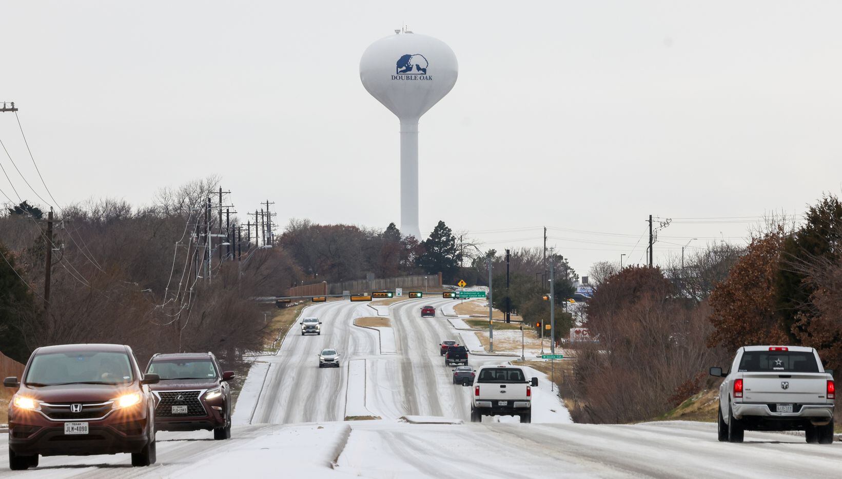 A Double Oak water tower overlooks cars driving slowly in the snow on Justin Road on Monday,...