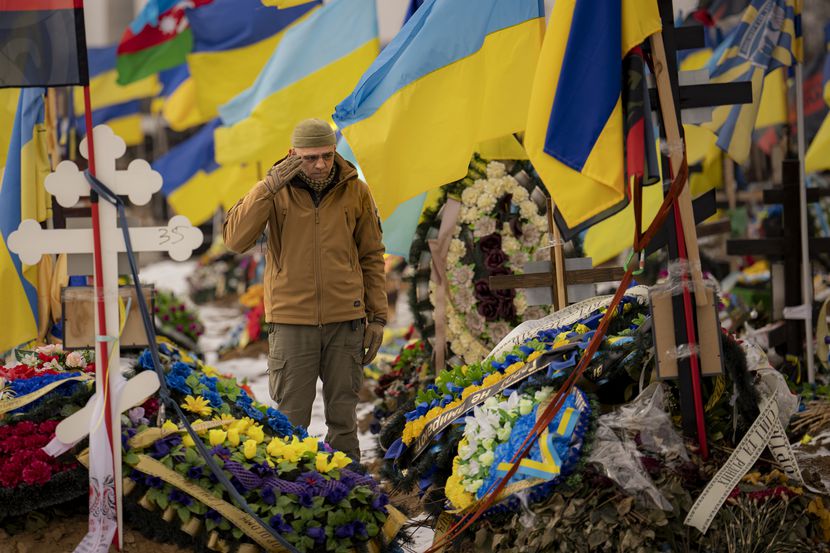 A Ukrainian serviceman salutes standing between the graves of soldiers during the funeral of...