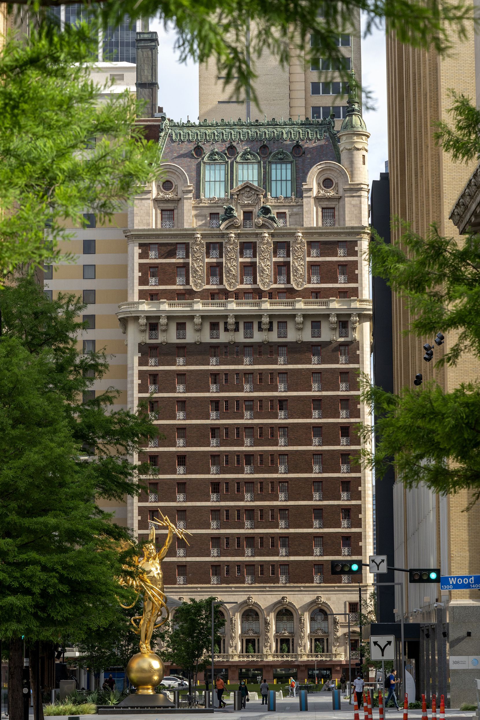 The Adolphus Hotel is seen through trees from the AT&T Discovery District. 