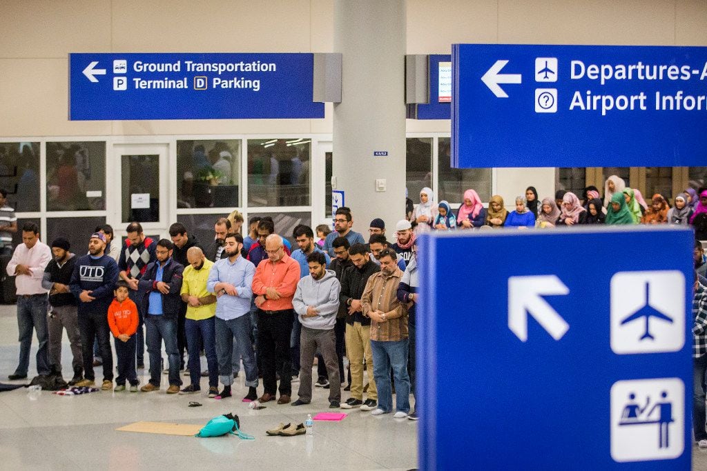 Muslim men set down their protest signs to pray at DFW International Airport where they...