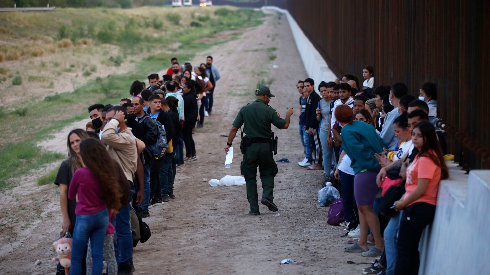 Un grupo de migrantes junto al muro fronterizo mientras un agente de la Patrulla Fronteriza...