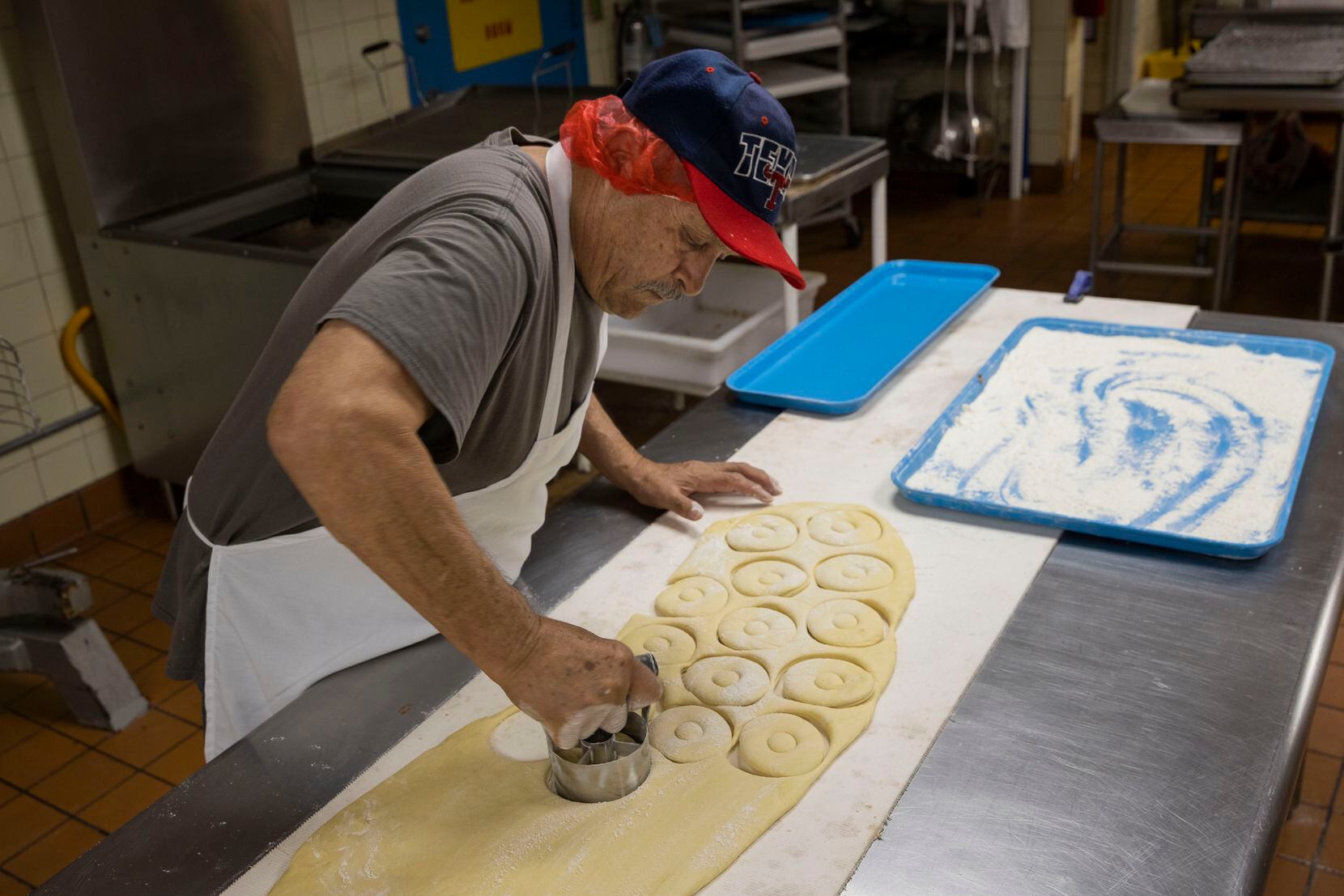 Tereso Mendoza, who has been working at Lone Star Donuts for over 30 years, cuts the donut...