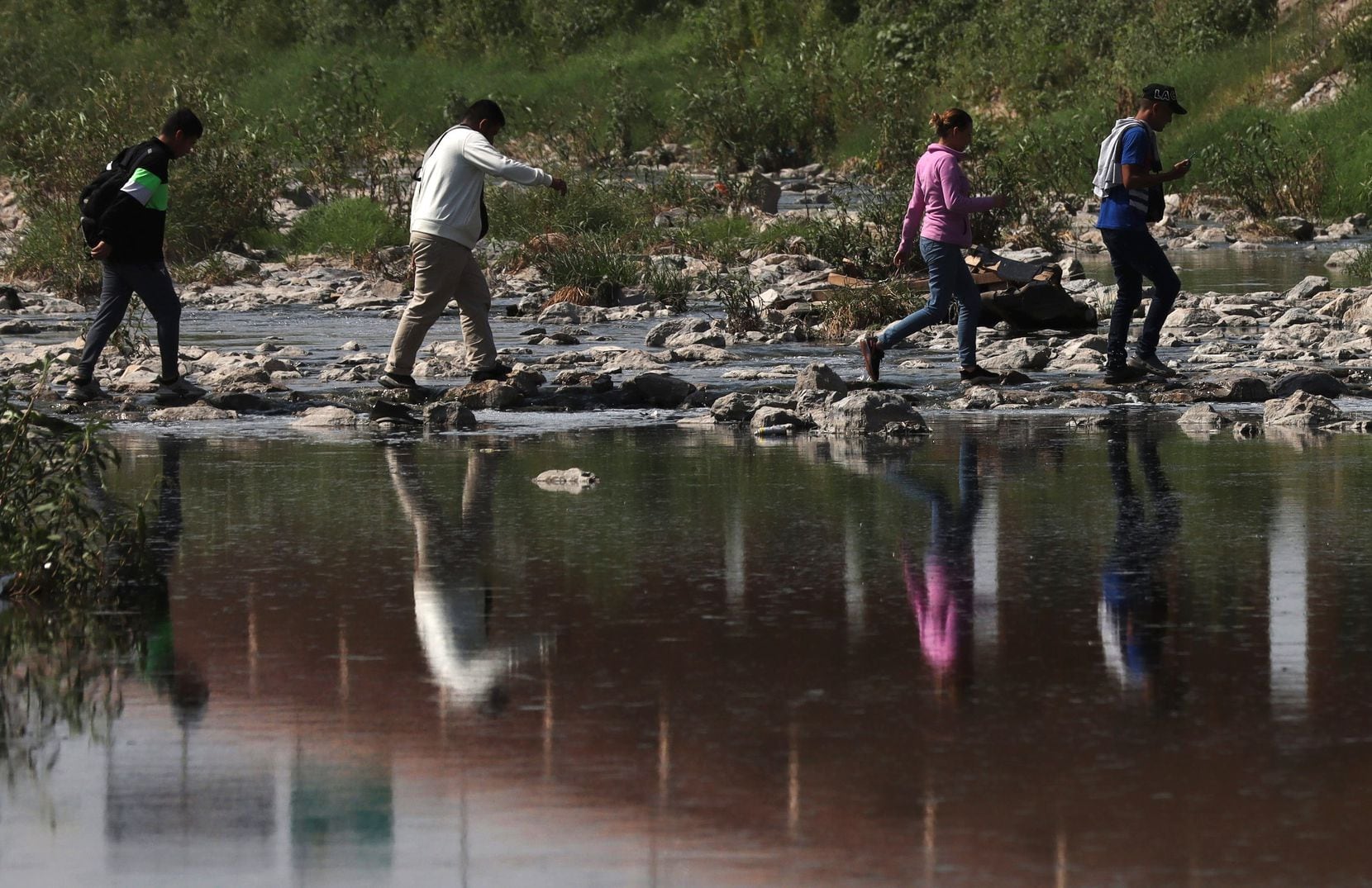 Migrants from several Latin American countries walk on the Rio Grande riverbed as they cross...
